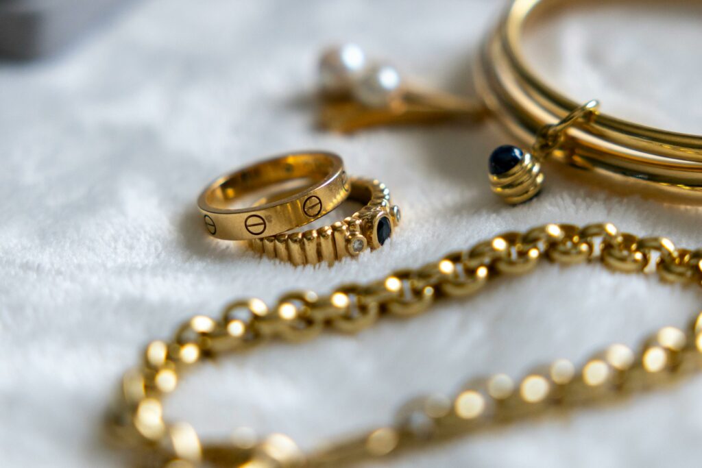 Collection of gold rings, bracelets, and chains with gemstones on a textured surface.