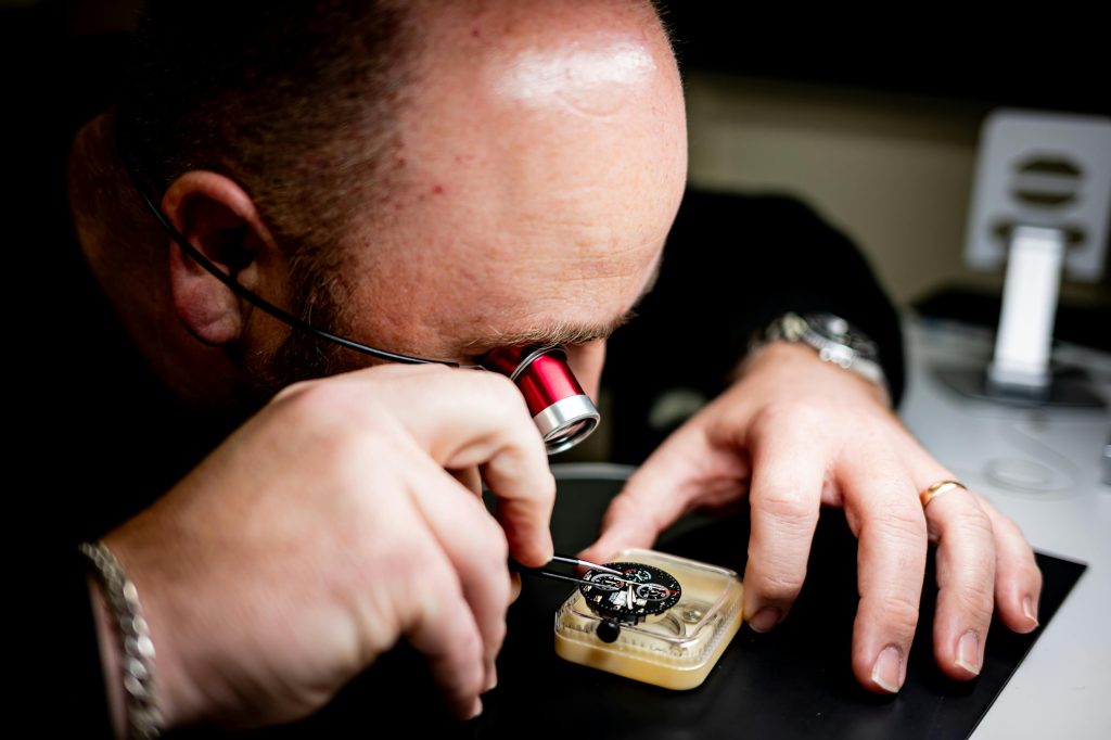 A professional watchmaker closely examines a watch mechanism with a magnifying glass.